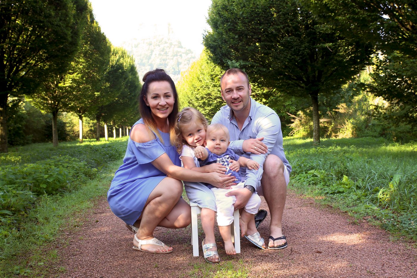 Glückliche Familie kniened vor Baumallee fotografiert