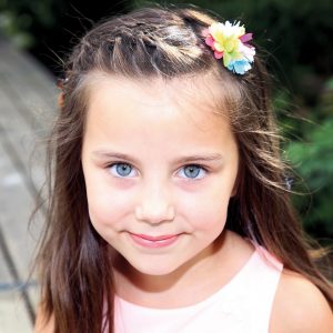 Mädchen mit strahlenden Augen und Blume im Haar fotografiert im Kindergarten