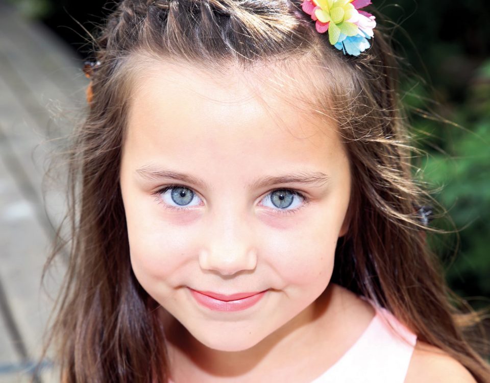 Mädchen mit strahlenden Augen und Blume im Haar fotografiert im Kindergarten