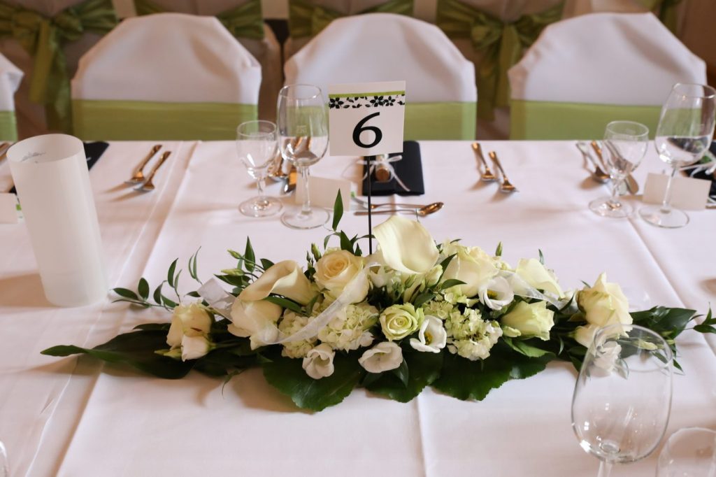 Blumengesteck auf Hochzeitstisch mit Tischnummer 8 in der Mitte und grünen Stuhlschleifen