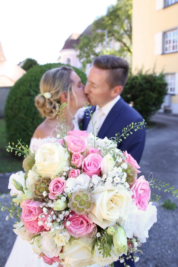 Brautstrauß im Vintage Stil mit küssendes Brautpaar im hintergrund