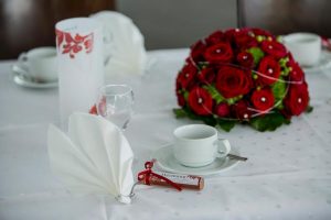 Blumen Tischgesteck in Rot neben einem Gastgeschenk